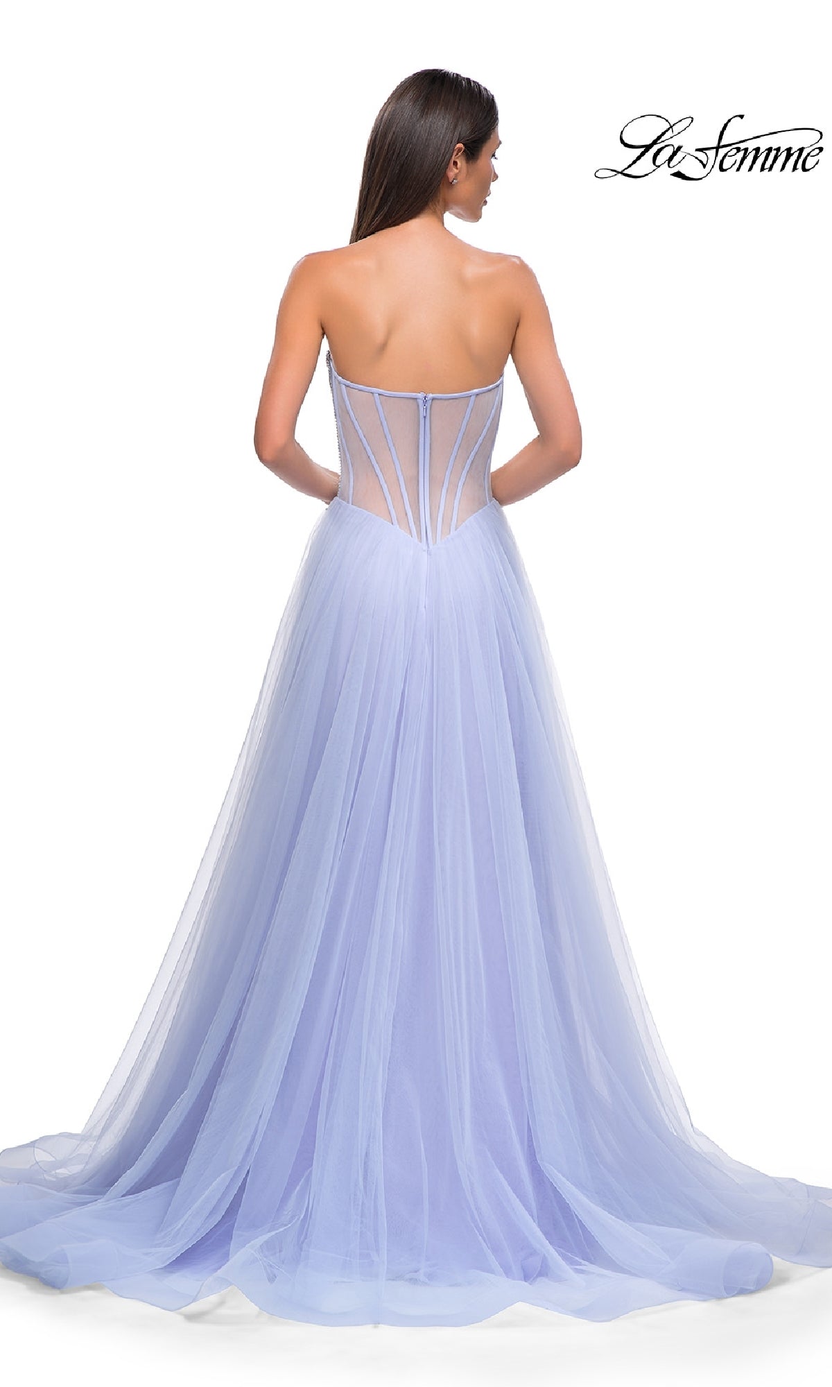A woman stands with her back to the camera in the Strapless Long Prom Ball Gown: La Femme 32811, featuring a floor-length lavender tulle skirt and a sheer beaded sweetheart corset-style back.